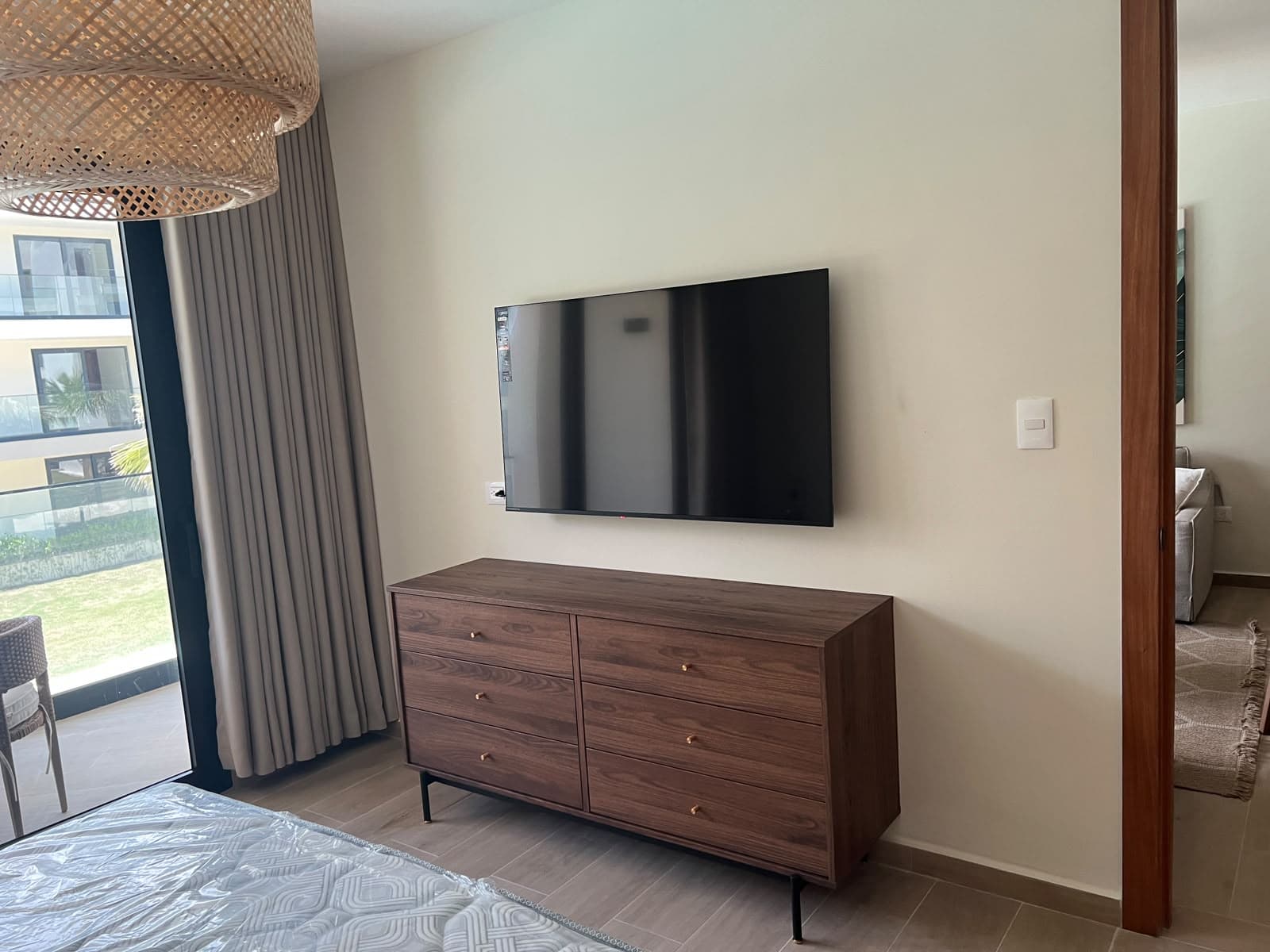 Walnut dresser beneath a wall-mounted television, with linen curtains at the balcony