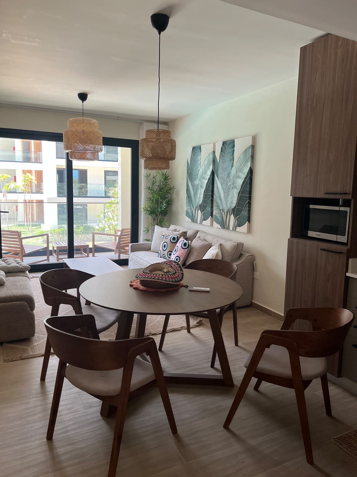Open-plan Dominican condo with a round dining table, linen sofa, rattan pendants, and a furnished balcony