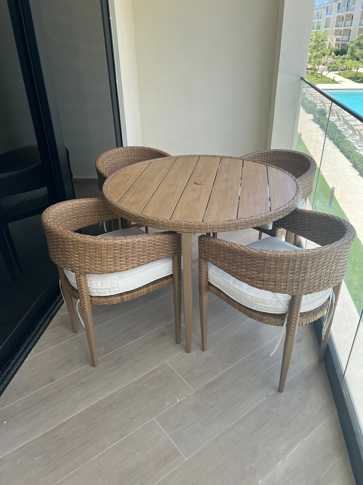 Round teak table and four wicker chairs with white cushions on a condo terrace